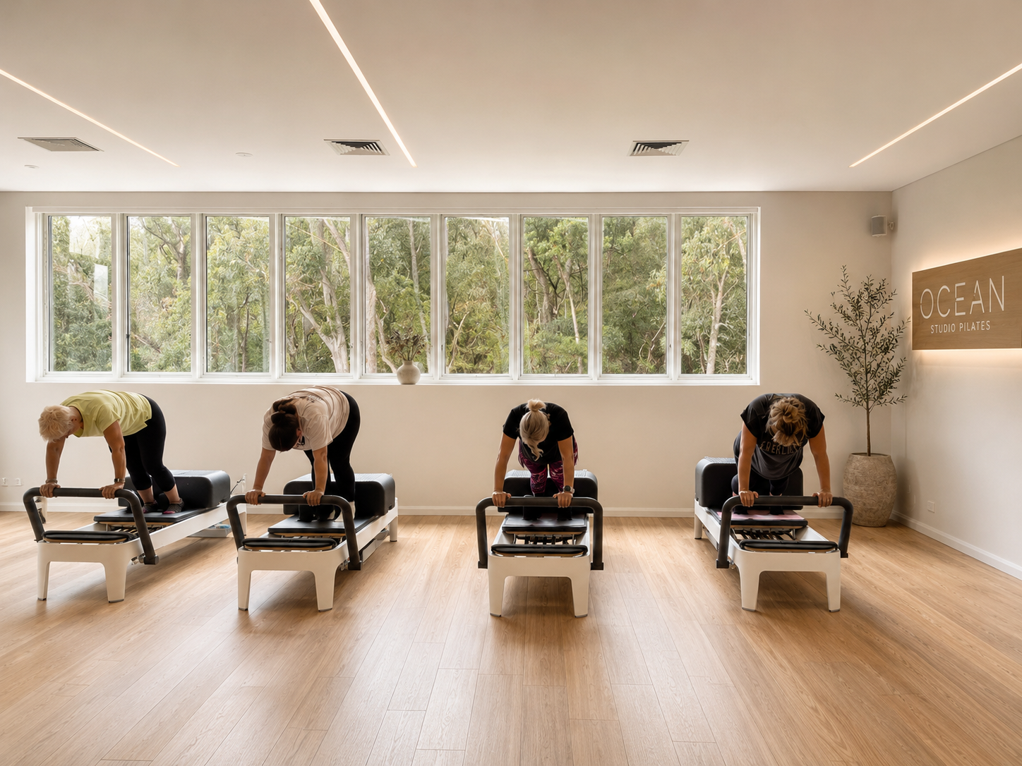 Four women working on Reformers beside the studio's tree-lined windows
